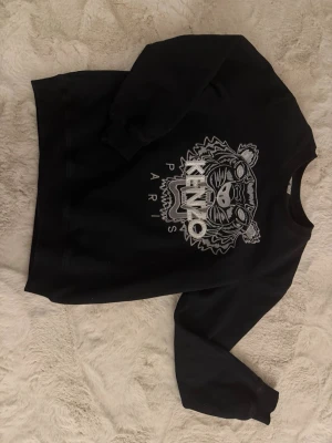 Svart Kenzo sweatshirt  - Fet svart sweatshirt från Kenzo med det ikoniska tigerhuvudet och texten 'KENZO PARIS' broderat framtill. Tröjan har rund halsringning och långa ärmar. Passar till alla stiler och till alla kläder
