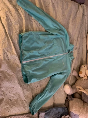 Turkos fleecejacka från Everest  - Mysig turkos fleecejacka från Everest med hel dragkedja framtill och hög krage. Perfekt att slänga på sig när det är lite kyligare. Tillverkad i mjukt fleecematerial och har en enkel, stilren design utan fickor på utsidan.