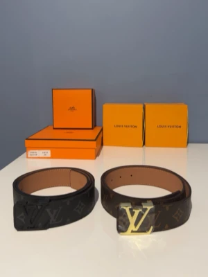 Louis Vuitton bälten - Louis Vuitton bälten med klassiskt monogrammönster. Ett är svart med mörka LV-detaljer och det andra är brunt med guld LV-spänne. Båda har bred design och exklusiv känsla, perfekta för att lyfta din outfit. 1 för 250 2 för 400. Aldrig använda