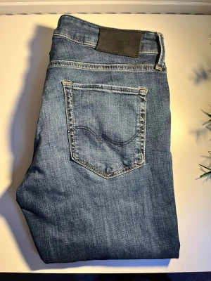 Blå jeans från Jack & Jones - Snygga blå jeans från Jack & Jones med klassisk femficksdesign och diskret slitning framtill. Jeansen har normal passform och är tillverkade i bomull med en liten mängd stretch för extra komfort. Perfekta för en avslappnad och trendig look.