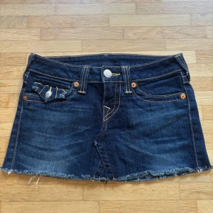 Mörkblå jeanskjol från True Religion - Säljer en mörkblå jeanskjol från True Religion med rå kant och snygga kontrastsömmar. Kjolen har klassiska fickor fram och bak med dekorativa knappar och broderade detaljer. Perfekt för dig som gillar street och denim. Köpte nyrligen från Plick men den passade tyvärr inte så nu säljer jag den vidare.