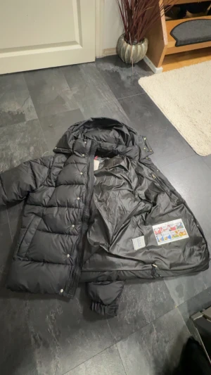 Svart Moncler pufferjacka S - Svart pufferjacka från Moncler med huva, quiltad design och flera fickor. Jackan har Moncler-logga på ärmen, dragkedja och tryckknappar framtill. Materialet är polyester och dun, perfekt för kalla dagar. Snygg och stilren look som funkar till allt.