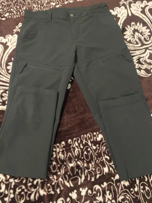 Svarta cargopants från Trekmates M - Svarta cargopants från Trekmates i storlek M. Byxorna har flera praktiska fickor med dragkedja och en stilren design. Perfekta för dig som gillar outdoor och vill ha funktionella byxor med cool look.