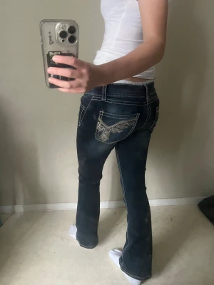 Mörkblå bootcut jeans med broderi - Snygga mörkblå jeans med bootcut passform och coola broderade detaljer på bakfickorna. Perfekt för dig som gillar en lite retro vibe och vill sticka ut med detaljer.