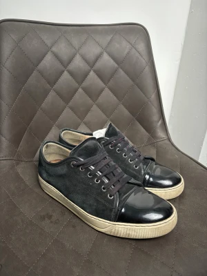 Lanvin - Säljer ett par exklusiva sneakers från Lanvin, kända för sin lyxiga design och höga kvalitet. Självklart äkta. Skorna är i svart mocka med svart lackad tå – en riktigt snygg och unik kombination som funkar både till vardag och mer uppklätt. Storlek 42. Bra 