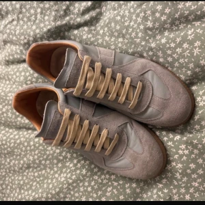 Maison Margiela sneakers Blå - Maison Margiela sneakers i blått med beige snörning och gummisula. Ovandel i mocka och skinn, med klassisk rund tå och platt sula. Insidan är fodrad i ljusbrunt skinn för extra komfort. Snygg retrostil som sticker ut med sin unika design.