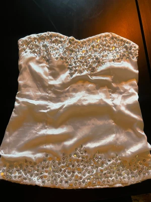 Vit tubtopp med paljetter - Säljer en glittrig vit tubtopp i satin med paljetter och pärlor upptill och nedtill. 