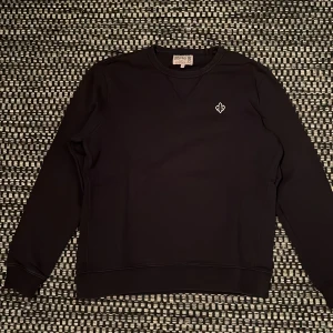 Mörkblå sweatshirt från Morris, S men sitter som S/XS - Mörkblå sweatshirt från Morris med broderad logga på bröstet. Tröjan har rund hals, ribbade muddar och lång ärm. Materialet är mjuk bomull och passformen är normal. Perfekt för dig som gillar stilrena och klassiska plagg med diskreta detaljer.