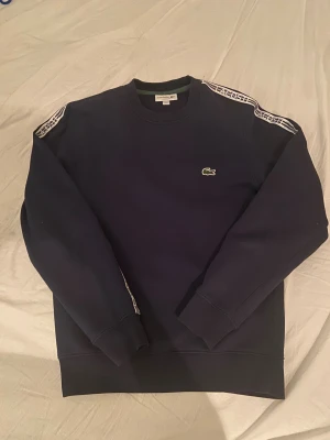 Mörkblå sweatshirt från Lacoste  - Säljer en Lacoste sweatshirt i bra skick som inte kommer till användning längre. Skriv om du har några funderingar eller vill ha fler bilder. Nypris: 1000kr