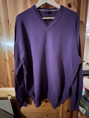 Lila v-ringad tröja från Atlant 2XL - Snygg lila tröja från Atlant i storlek 2XL. V-ringad hals med ribbade muddar vid ärmslut och nederkant. Tröjan har lång ärm och är tillverkad i mjukt material som känns skönt mot huden. Perfekt för dig som gillar enkel och stilren design.