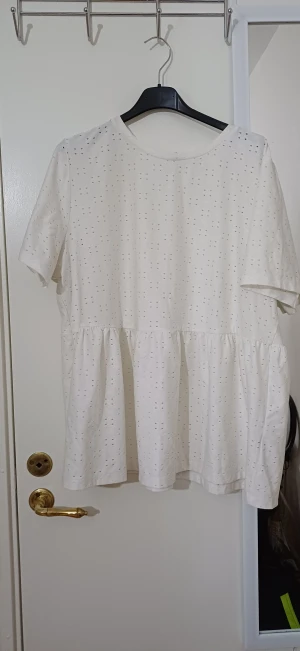 Vit blus med broderade hål från Esmara - Säljer en vit blus från Esmara i storlek XL. Blusen har korta ärmar, rund hals och ett sött broderat hålmönster över hela tyget. Den har en volang nedtill som ger en luftig och avslappnad vibe. Perfekt för dig som gillar ljusa och feminina toppar.
