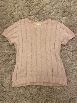 Ljusrosa stickad tröja Gina Tricot - Supersöt ljusrosa stickad tröja från Gina Tricot med korta ärmar och klassiskt flätmönster. Rund halsringning och ribbade muddar vid ärmslut och nederkant. Perfekt för dig som gillar mjuka och mysiga plagg.