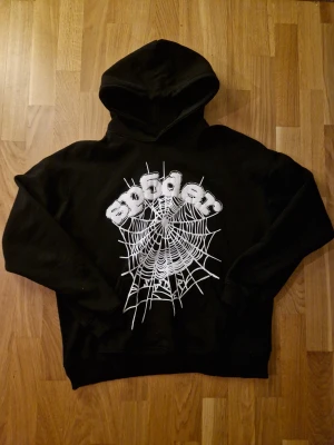 Svart Spider hoodie med spindelnätsprint - Svart hoodie från Spider i storlek L med stor vit spindelnätsprint och 3D-broderad text på bröstet. Tröjan har huva och långa ärmar, tillverkad i 100% bomull. Perfekt för dig som gillar streetwear och coola detaljer. Knappt använd !! Passar mer M!!!