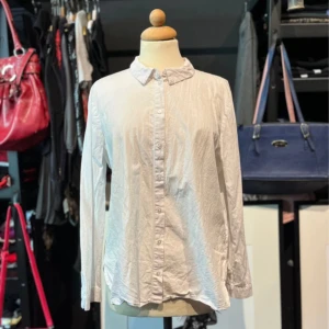 Vit klassisk skjorta  - Vit skjorta i klassisk modell med krage och knäppning framtill. Långärmad med manschett och knappar vid ärmslut. lätt och luftig med rundad nederkant. Perfekt för en clean och stilren look.