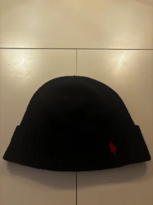 Mörkblå Ralph Lauren mössa - Mörkblå Ralph Lauren mössa i 100% merinoull. Knappt använd. Tveka inte på att höra av dig vid minsta lilla fundering!