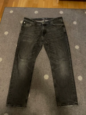 Tommy Jeans svarta straight jeans W32 - Säljer ett par svarta Tommy Jeans i klassisk straight fit. Jeansen har snygga slitningar, fem fickor och tydliga logodetaljer både fram och bak. Materialet är robust denim med en cool tvättad look och röda sömmar på insidan. Perfekta för dig som gillar streetwear.