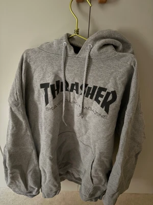 Grå Thrasher hoodie  - Säljer en grå hoodie från Thrasher med klassiskt svart logotryck på bröstet. M/L