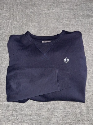 Mörkblå sweatshirt från Morris - Snygg mörkblå sweatshirt från Morris med rund hals och broderad vit logga på bröstet. Strl M. Tröjan har långa ärmar och ribbade muddar vid ärmslut och nederkant. Perfekt för dig som gillar stilrena och klassiska plagg. Kan tänka mig och gå ner lite i pris vid snabb affär. Hör av er vid intresse/ frågor!