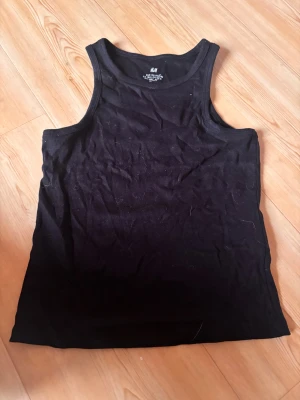 Svart och vit ribbad linnetopp H&M - Två ribbade linnetoppar från H&M i storlek 170/US 20. Ena toppen är svart och den andra är vit, båda med klassisk rund hals och ärmlös design. Perfekt för layering eller att bära som de är. Materialet är mjukt och stretchigt för skön passform.