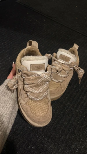 Beige UGG sneakers lowmel - Säljer mina UGGs sneakers lowmel i färgen ”beige” i strl. 36. Skorna har breda snören med diskret mönster, detaljer i mocka och textil samt äkta fårull. Såå sköna och VARMA på vintern. De är impregnerade 2 gånger så ni behöver inte oroa er för fläckar från vatten eller salt! De är i väldigt fint skick. Enda är små fläckar från jeans (se på bilderna) men inget som syns på håll. Ord. Pris ca 2900kr. Bara och höra av er vid frågor!🩷