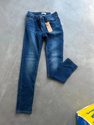 Nya Slim fit blå jeans från Lindex - Snygga blå jeans från Lindex i slim fit-modell med smal passform och tighta ben. Klassisk femficksdesign, justerbar midja och Detroit-knapp. Jeansen har en fräsch tvätt med lätt slitning och är tillverkade i bomullsmaterial.