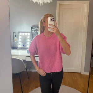 Rosa stickad tröja med puffärm - Superfin rosa stickad tröja med korta puffärmar och rund hals. Tröjan har en ribbad kant vid ärmslut och nederkant, vilket ger en snygg och trendig look. Perfekt att styla med jeans eller kjol för en färgglad outfit.