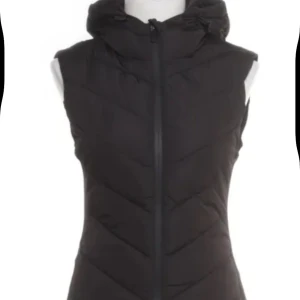 Svart dunväst från Zara med luva - Svart dunväst från Zara med snygg quiltad design och dragkedja framtill. Västen har en hög krage och en  luva, perfekt för lager-på-lager-stil. Passformen är figurnära och västen är enkel att matcha till olika outfits.