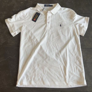 Helt ny pikétröja från polo Ralph lauren - Snygg vit pikétröja från Polo Ralph Lauren med klassisk krage och korta ärmar. Tröjan har knappar framtill och den ikoniska broderade loggan på bröstet. Perfekt för dig som gillar stilrena och tidlösa plagg.