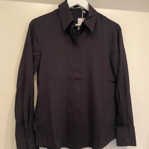 Svart skjorta från Mango - Elegant svart långärmad skjorta med klassisk krage och dolda knappar framtill. Perfekt för en stilren look.