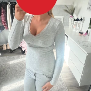 Ljusgrå ribbad långärmad tröja - Säljer en ljusgrå ribbad långärmad tröja med v-ringning och spetskant. Tröjan har en slim passform och är perfekt för dig som gillar en enkel men ändå söt stil. Supermjuk och skön att bära till jeans eller kjol.