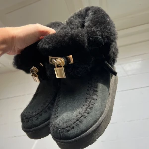 Svarta UGG -liknande boots  - Unika svarta boots med fluffig päls runt skaftet och snygga guldfärgade låsdetaljer framtill. Skorna är inköpta i Italien från ett fint märke och är i gott skick!