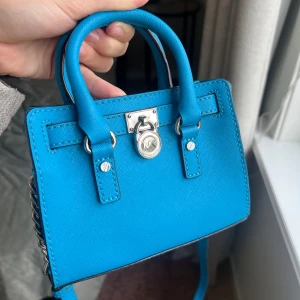 Hamilton Michael Kors väska mini - Säljer min fina Michael Kors Hamilton-väska i Saffiano-läder. Den är använd endast ett par gånger och har inga tecken på användning – ser i princip ny ut!  👜 Detaljer: 	•	Modell: Hamilton 32T2SHMM1Y 	•	Material: Saffiano-läder (hållbart, reptåligt och vattenavvisande) 	•	Storlek: Mini PRIS KAN DISKUTERAS‼️