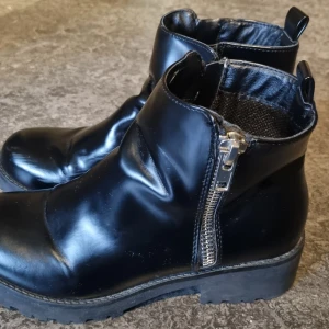 Svarta boots från Vox Sko, storlek 39 - Snygga svarta boots från Vox Sko i storlek 39. De har en rund tå, platt sula och dragkedja på sidan för enkel på- och avtagning. Tillverkade med robust yttersula som ger bra grepp. Perfekt för dig som gillar stilrena och praktiska skor. Observera vissa märken på skorna. Se bilder