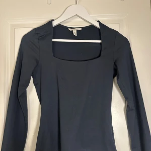 Mörkblå långärmad topp från H&M - Säljer en stilren mörkblå långärmad topp från H&M med fyrkantig urringning. Toppen är figurnära och har en enkel, clean design som passar perfekt till jeans eller kjol. Tillverkad i mjukt och stretchigt material för en bekväm passform.