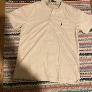 Beige Polo t-shirt från Ralph Lauren - Snygg beige t-shirt från Polo Ralph Lauren med klassisk pikékrage och två knappar framtill. Den har korta ärmar och den ikoniska broderade loggan på bröstet. Perfekt för dig som gillar stilrena och tidlösa plagg. Det är fast pris!