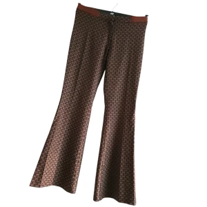 Bisou Bisou byxor, stl 38–40, utsvängda - Stilrena och bekväma byxor med utsvängda ben och ett elegant mönster i bruna toner. Kvaliteten känns lyxig och de sitter snyggt på kroppen.  Märkta stl 42, men passar ev bättre 38–40 beroende på passform. Perfekta till både vardag och fest!