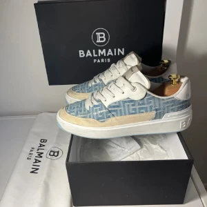 Balmin b-court sjukt unika - Snygga Balmain sneakers i blått och vitt med mönstrad textil och detaljer i mocka och skinn. Platt sula med Balmain-logga undertill, snörning och rund tå. Perfekt för dig som gillar exklusiv streetstyle och vill sticka ut med ett lyxigt märke.