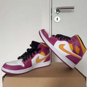 Nike Air Jordan 1 Familia lila/gul - Nike Air Jordan 1 Familia sneakers i lila, vitt och gult med coola kontrastsömmar och broderad Swoosh. Skon har svart snörning, rund tå och platt sula. 'FAMILIA' tryckt på tån och Air Jordan-logga på sidan. Perfekt för dig som vill sticka ut med färg och stil.