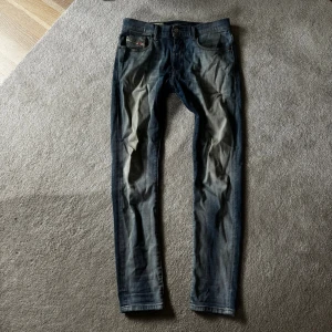 Tvärfeta Diesel Jeans👖 - Snygga blå jeans från Diesel med coola slitningar och ljusa tvättade partier framtill och baktill. Klassisk femficksmodell med läderpatch bak i midjan och röda detaljer vid fickan. Jeansen har rak passform och är tillverkade i mjukt denimtyg.