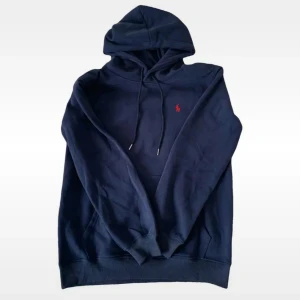 Marinblå hoodie från Polo Ralph Lauren - Säljer en marinblå hoodie från Polo Ralph Lauren med röd logobroderi på bröstet. Tröjan har huva med snörning, magficka och långa ärmar. Mjuk och skön bomullskvalitet, perfekt för chill dagar. Passar dig som gillar klassisk streetstil. Inte riktigt!!