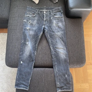 Svarta distressed jeans från Dsquared2 - Säljer ett par svarta jeans från Dsquared2 med coolt distressed och slitna detaljer. Jeansen har fem fickor, knappgylf och smal passform. Materialet är klassisk jeans och färgen är tvättad svart med ljusa partier och råa kanter.