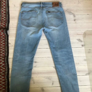  Lee slimfit jeans  - Snygga ljusblå jeans från Lee med klassisk femficksdesign och brunt Lee-läderpatch bak. Jeansen är slim fit storlek W31 L32 med subtila slitningar. Perfekt för dig som gillar en clean och modern look.
