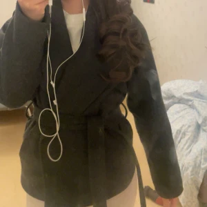 Svart omlottkappa med bälte - Säljer en svart kappa i omlottmodell med bälte i midjan. Jackan har en stilren och enkel design med bred krage och långa ärmar. Perfekt för dig som gillar en clean look och vill ha något som funkar till många outfits. Den är från only köpte förra året. 