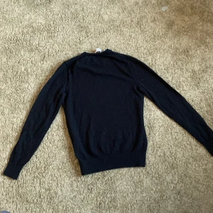 Svart stickad tröja Tiger of Sweden - En svart, klassisk stickad tröja från Tiger of Sweden. Tröjan har rund halsringning och långa ärmar, perfekt för lager-på-lager under kyliga dagar. Enkel och stilren design som funkar till det mesta.