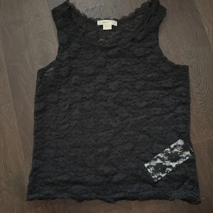 Svart spetslinne från Gina Tricot - Säljer ett svart, ärmlöst linne från Gina Tricot i storlek 146/152. Linnet är helt i genomskinlig spets med blommigt mönster och har en mjuk, stretchig känsla. Perfekt för att skapa en cool lager-på-lager-look. Funkar även i storlek för mig som är 158/164.