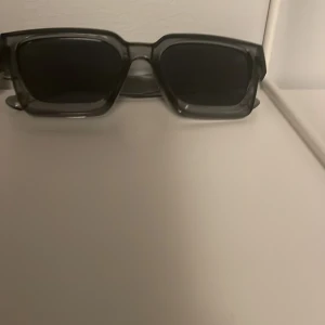 Svarta solglasögon - Snygga svarta solglasögon med rektangulär form och tjock plastbåge. Perfekt accessoar för att ge din look en cool edge. Glasen är mörka och bågarna har en modern, stilren design.