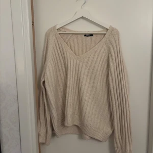 Beige ribbstickad tröja V-ringad - Mysig beige stickad tröja från Bik Bok med bred v-ringning och ribbad struktur. Tröjan har lång ärm och en loose passform som ger en avslappnad vibe. Perfekt för lager-på-lager under höst och vinter.