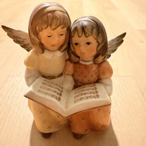 Goebel Änglar med Notbok Porslinsfigur - Vacker Goebel porslinsfigur föreställande två änglar som sjunger ur en notbok. Fint skick med små spår av normalt slitage, inga synliga sprickor. Perfekt för samlare eller som dekorativ inredningsdetalj.