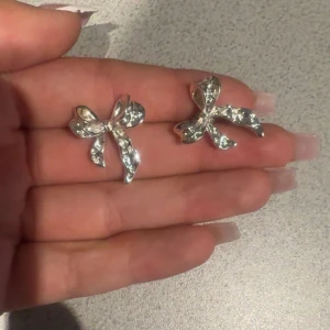 Glittriga rosettörhängen i silver - Supersöta örhängen i form av rosetter, helt täckta av glittrande stenar. De är i silverfärg och har en snygg, feminin design som verkligen poppar. Perfekta för dig som vill ha något extra till din look. Knappast använda och nyligen köpta🫶🏽