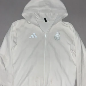 Vit hoodiejacka Real Madrid Adidas - Köpt i unisport för 1099kr och har använts några gånger. Vill sälja den nu för att den används inte mer.